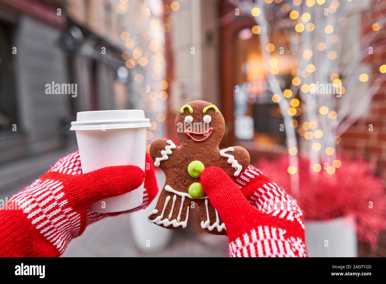 Hand in red mitten holding coffee cup and a smiling gingerbread man