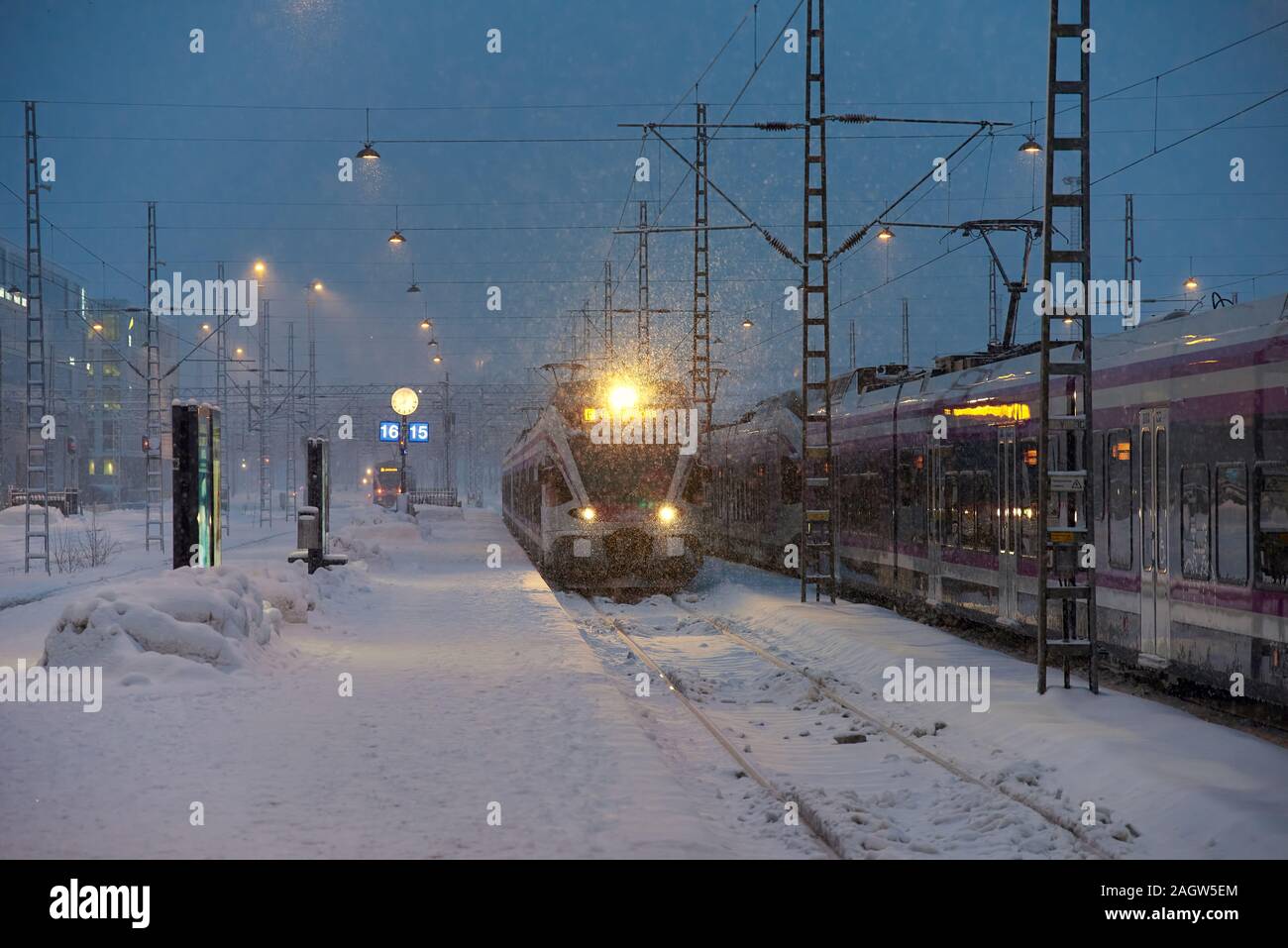 Helsinki, Finland - February 6, 2019: A local commuter train arriving at the Helsinki central railway station in heavy snow storm just before dawn in Stock Photo