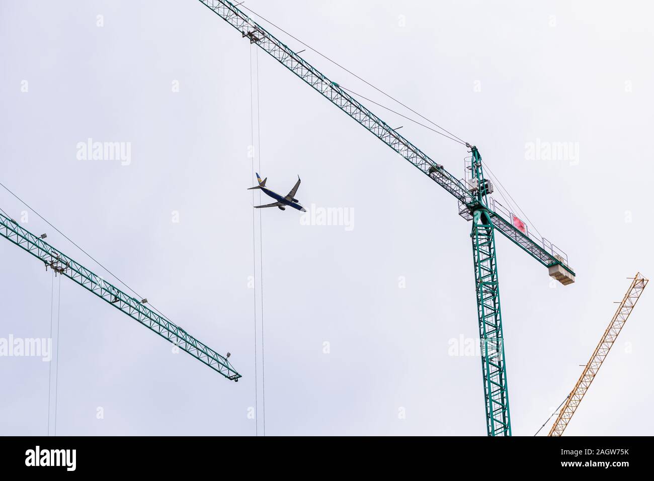 Valencia, Spain - December 20, 2019: Ryanair plane flies over the city framed among building construction cranes, cities grow with tourism. Stock Photo