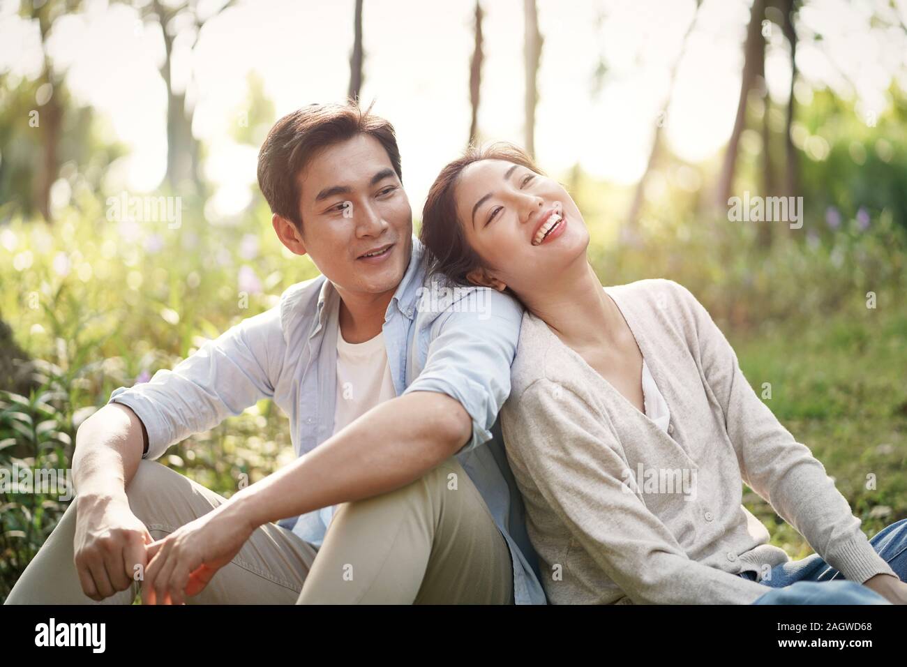beautiful happy young asian couple sitting on grass talking chatting relaxing in park Stock Photo