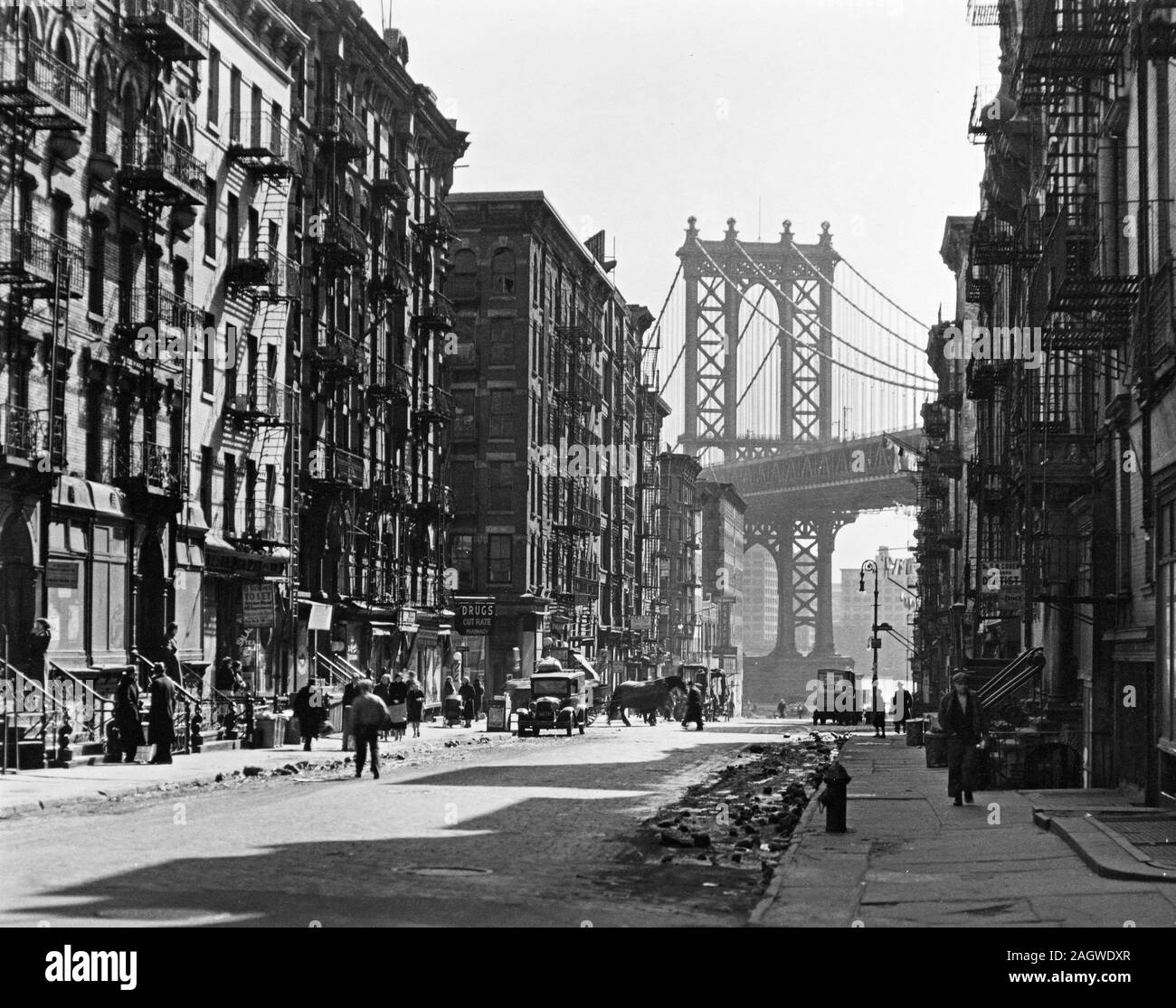 Looking down Pike Street toward the Manhattan Bridge, street half in shadow, rubble in gutters, some traffic. Pike and Henry Streets, Manhattan. ca. 1936 Stock Photo