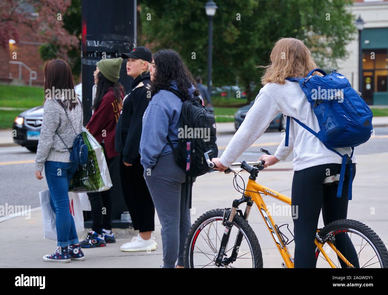 Storrs, CT USA. Oct 2019. Caucasain female student on bicycle waiting at campus intersection with diverse group of Hispanic and Asian students. Stock Photo