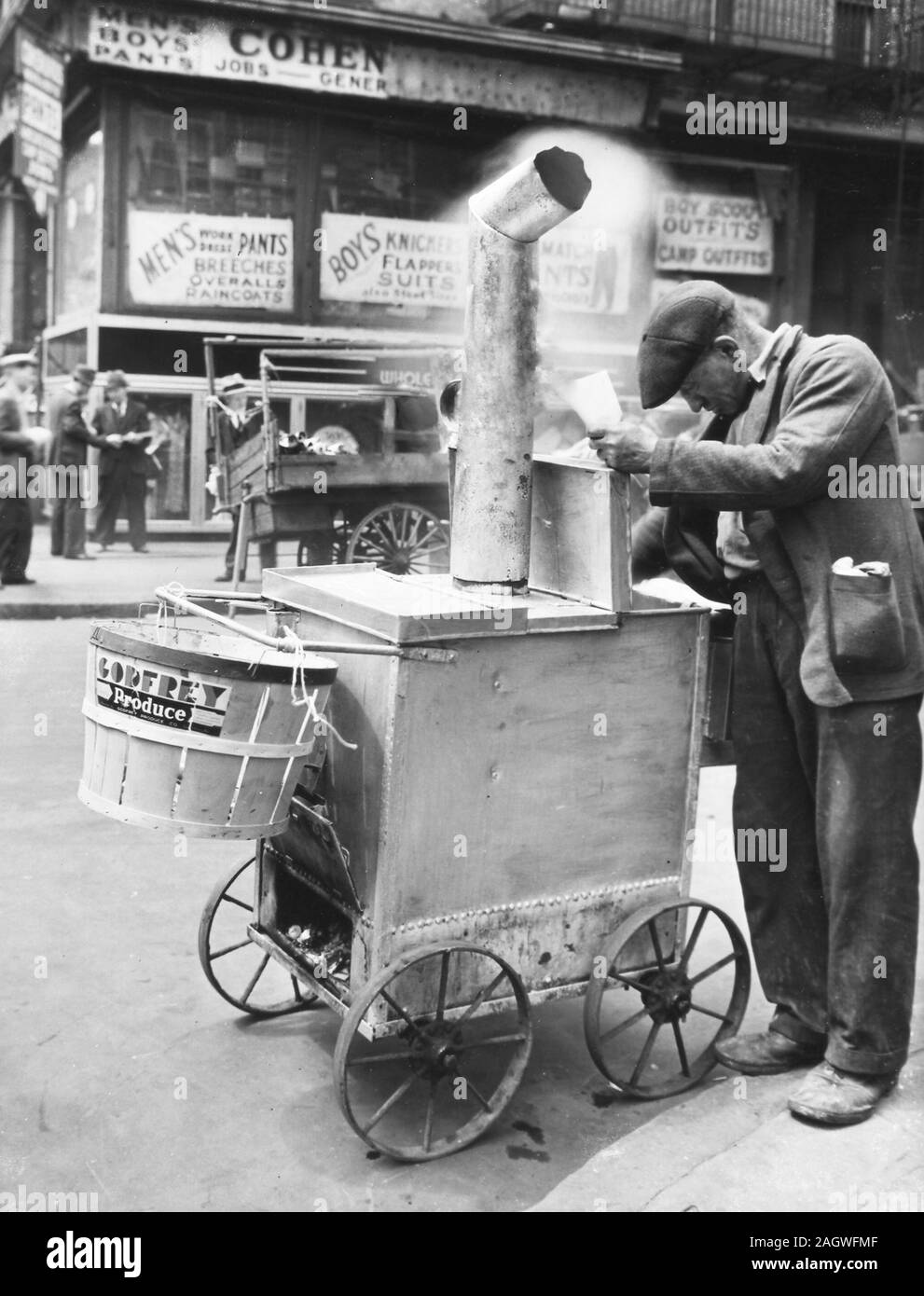 Roast corn man peering into cart, basket on the front; other peddlers, clothing stores, beyond. Stock Photo