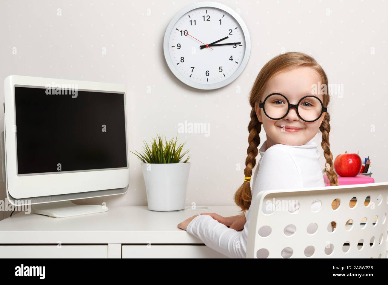 Cheerful cute little girl a schoolgirl with glasses sits at a table ...