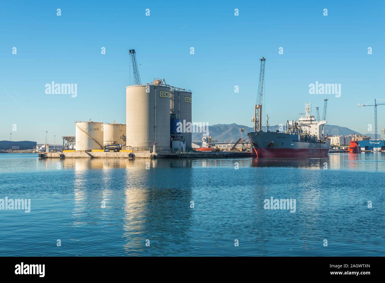 Malaga, Spain - December 4, 2018: Cement Carrier Vessel Glory Tellus and bulk storage of concrete cement silos and Bacardi tanks at entrance of Malaga Stock Photo
