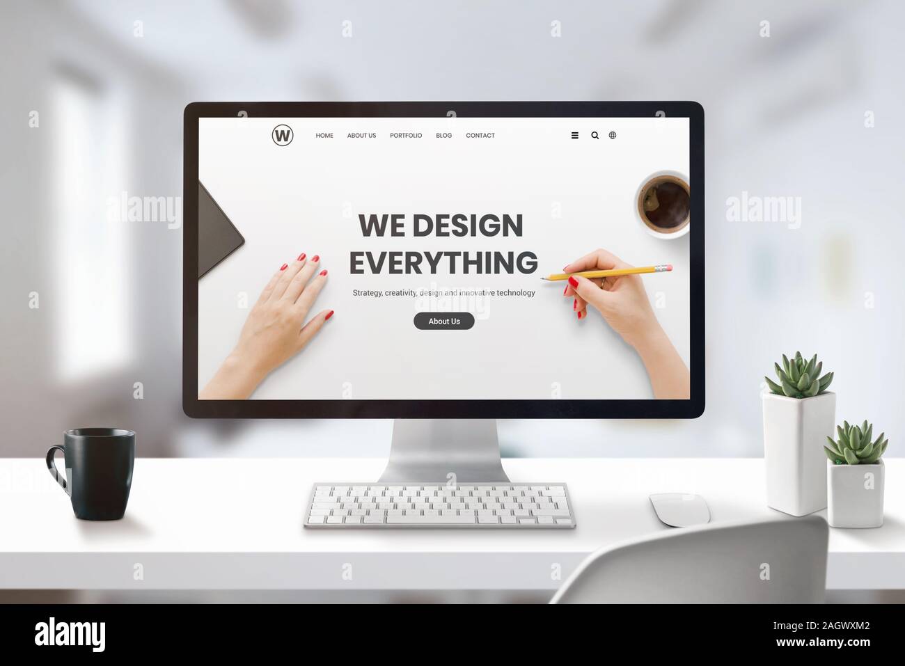 Web design studio concept with modern agency web page on computer display. Office, studio desk with cup of coffee and plants beside Stock Photo