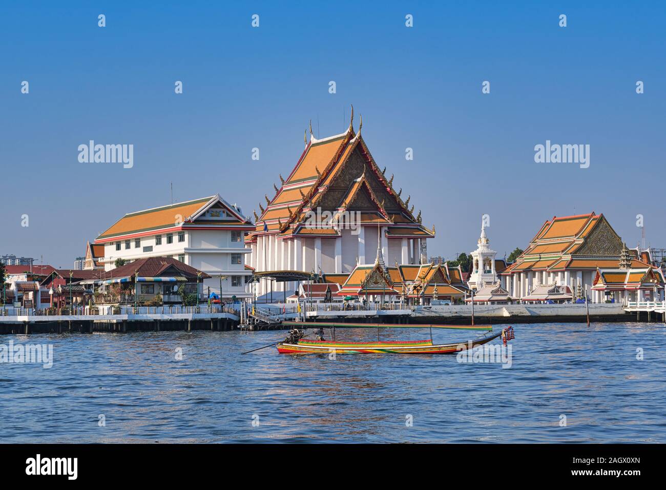 A so-called long-tail boat on the Chao Phraya River in Bangkok, Thailand with (temple) Wat Kalayanamit in the background Stock Photo