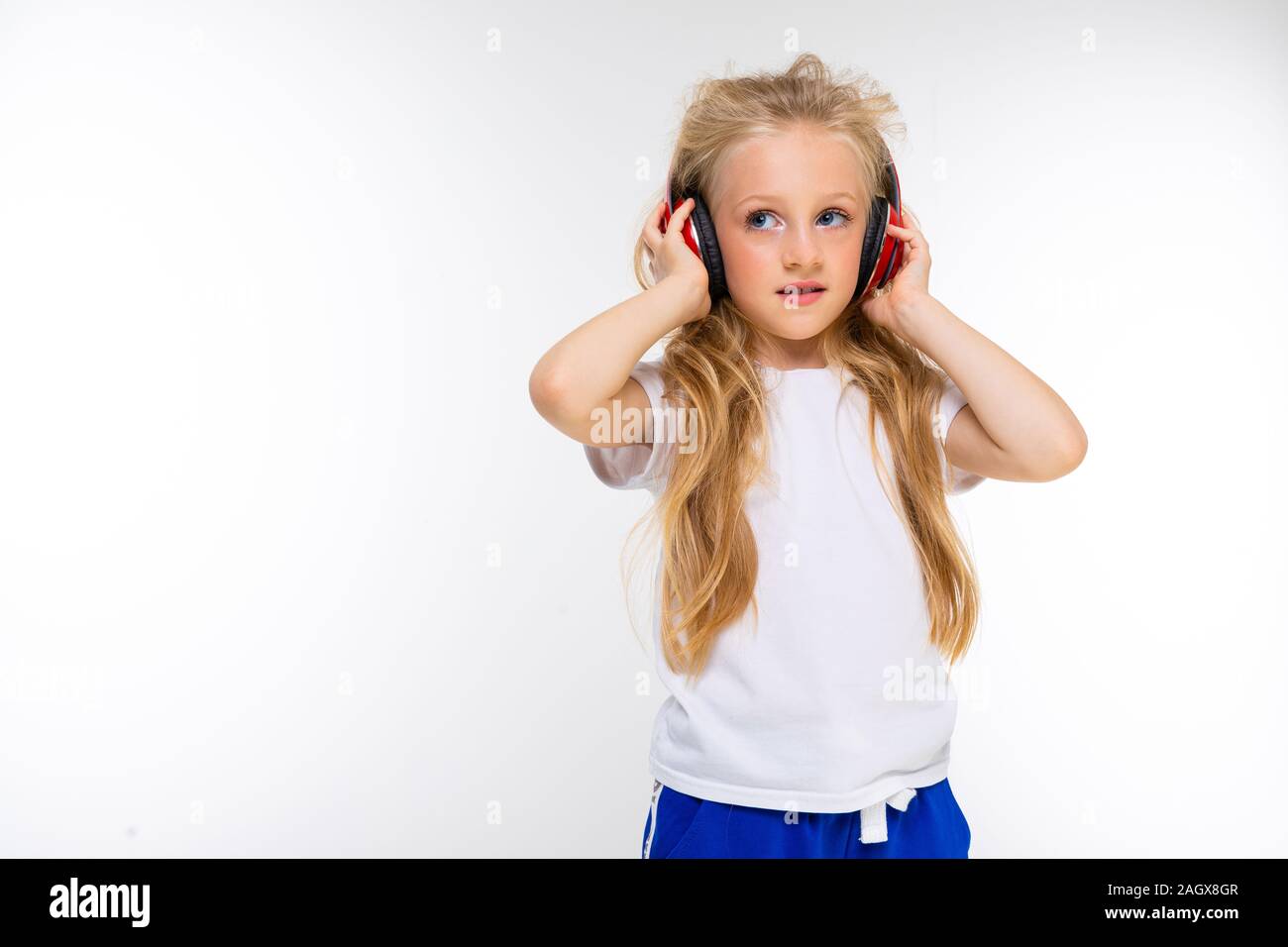 portrait of a beautiful blond charming young cute girl in a casual look with red headphones and on a white background Stock Photo