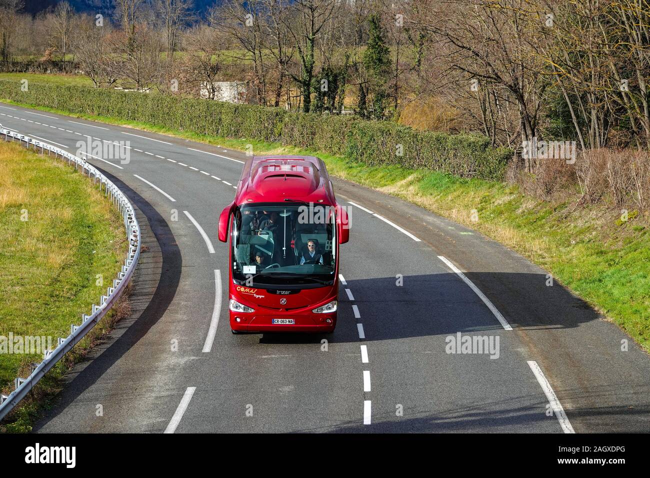 Big red bus driving on the right on dry road with bend, France Stock Photo