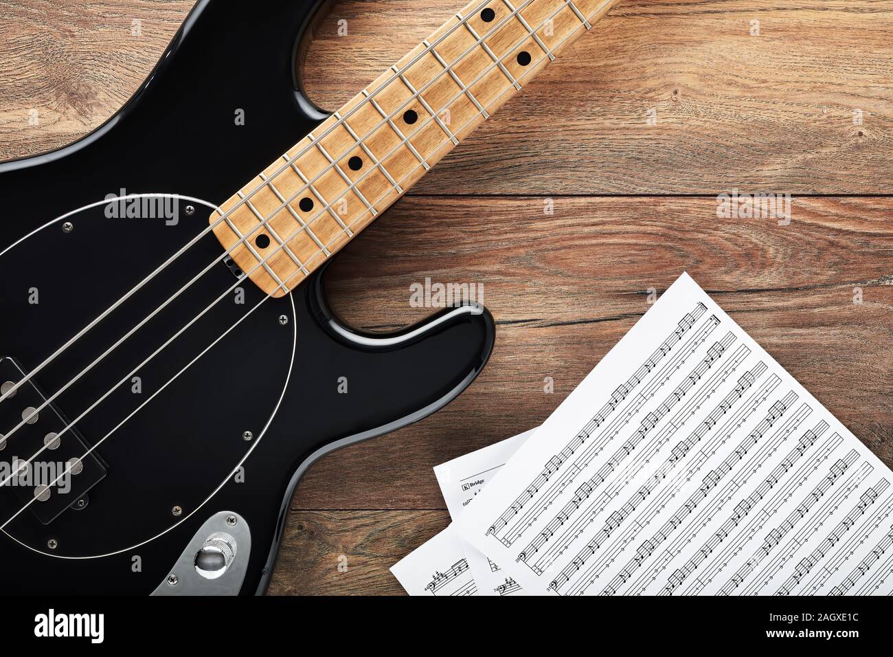 Black bass guitar with headphones and sheet music on wooden table. Music production, composing or practicing. Stock Photo