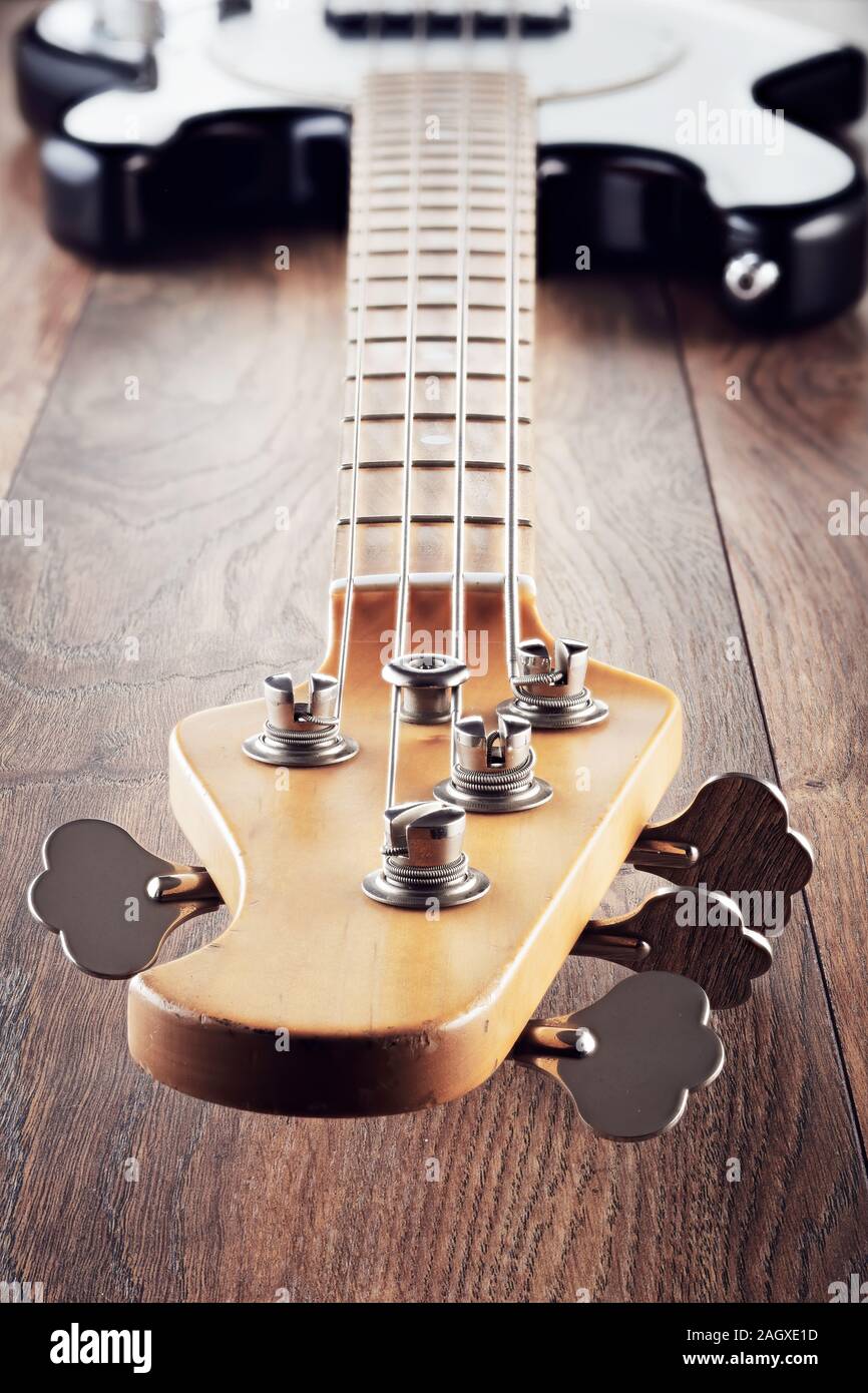 Vintage electric bass guitar on wooden table background. Vanishing view from the headstock or neck up the body. Close up view. Stock Photo