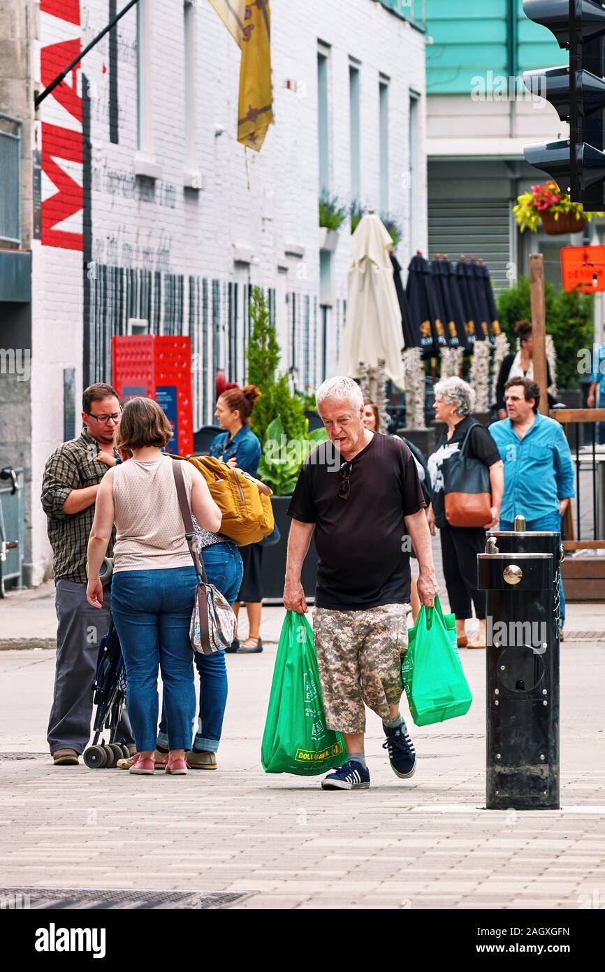 Montreal, Canada - June, 2018: Canadian old man carrying plastic shopping bags on the crowded street in Montreal, Quebec, Canada. Stock Photo