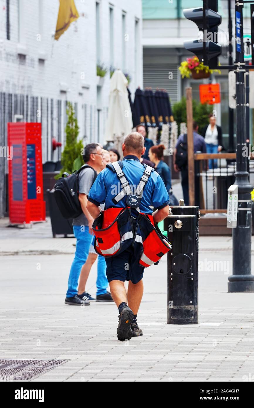 Montreal, Canada - June, 2018: Facing back Canadian mailman courier carrying bags on the street. Stock Photo
