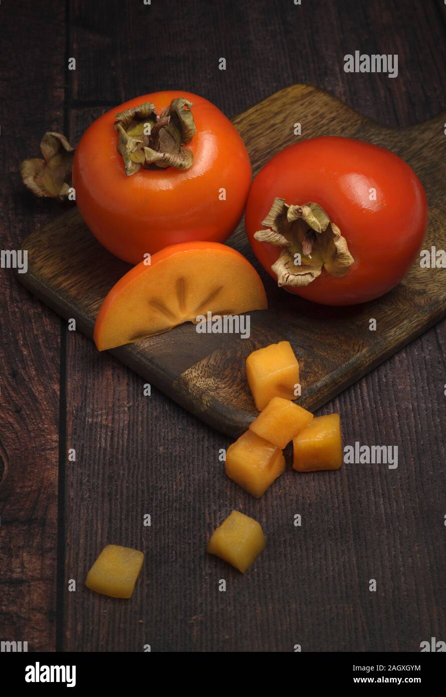 Fresh ripe persimmons on wooden cutting board Stock Photo