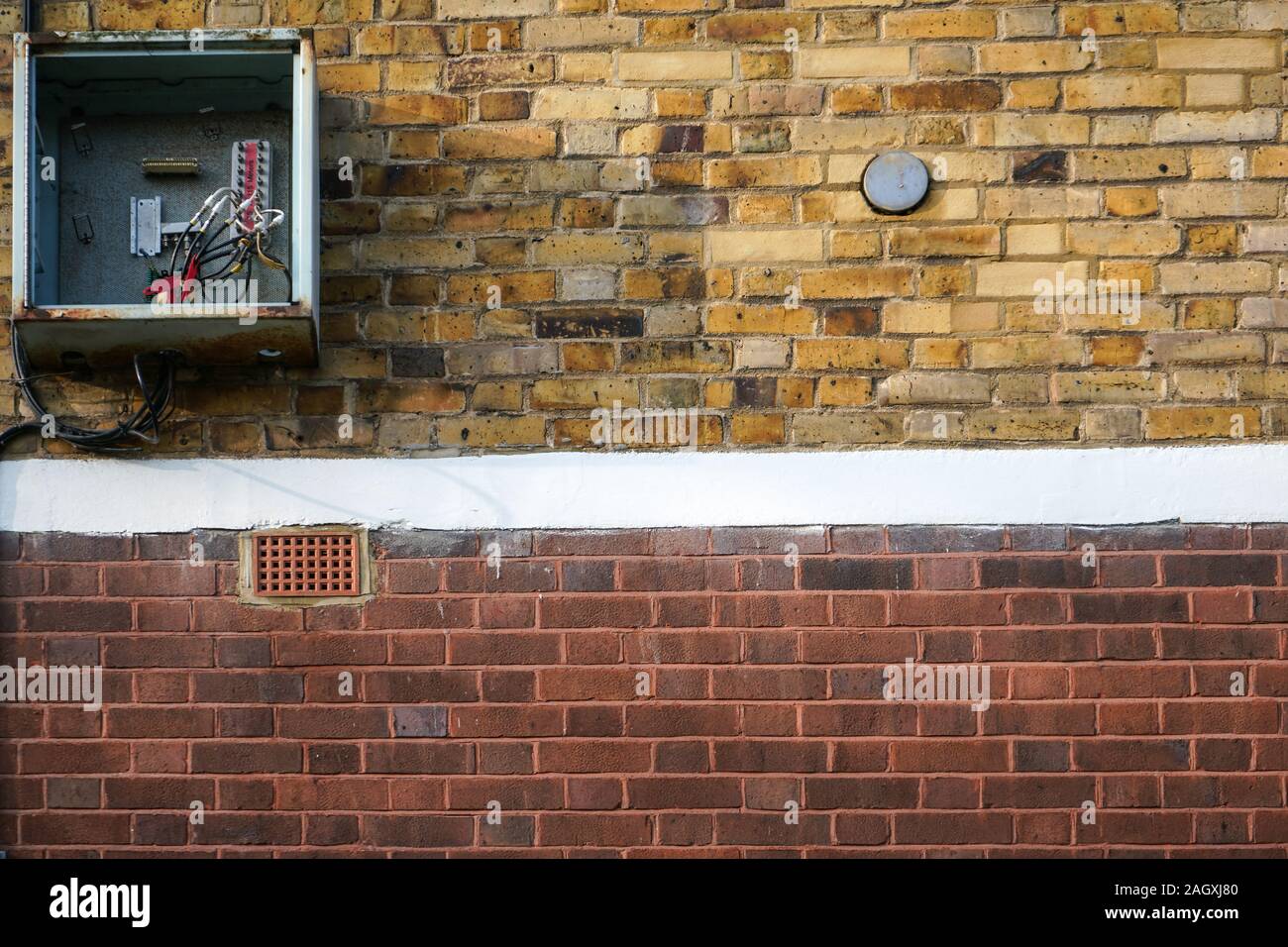 Bricks wall, with electricity / fuse box on it, opened, cover missing, cables visible. Stock Photo