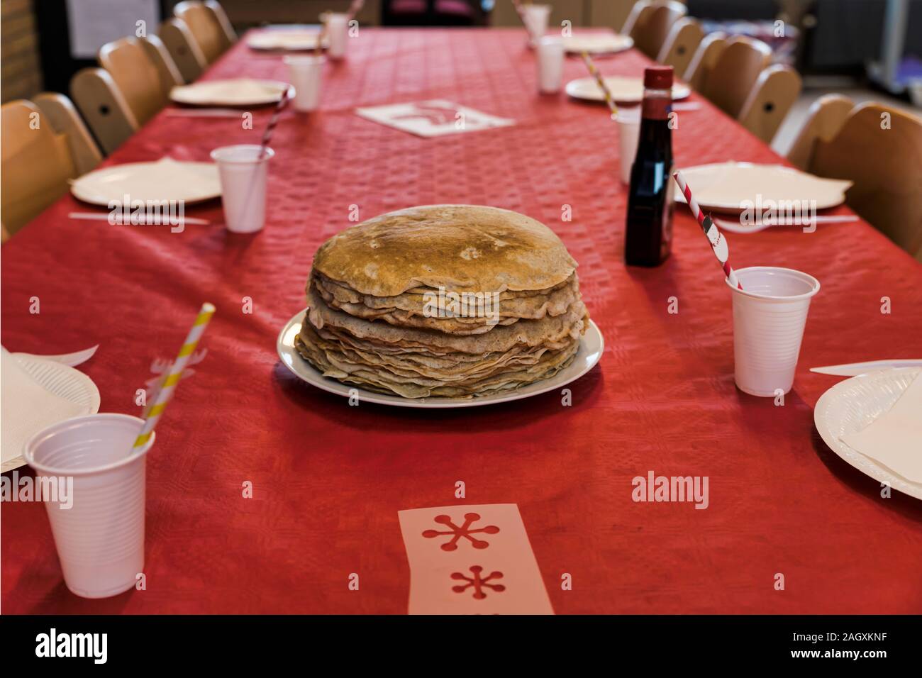 set table with a plate with a stack of pancakes on a red tablecloth with cups for drinks Stock Photo