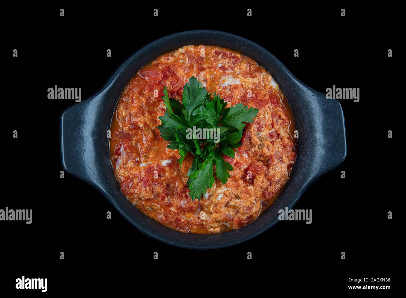 Traditional turkish menemen, made by eggs, tomatoes and various spices. Menemen dinner in cast pan on black background. Stock Photo