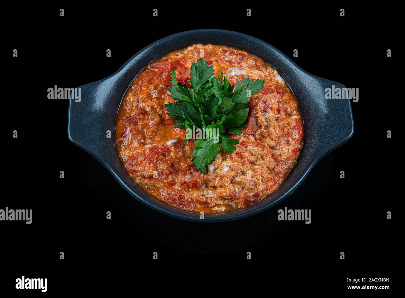 Traditional turkish menemen, made by eggs, tomatoes and various spices. Menemen dinner in cast pan on black background. Stock Photo