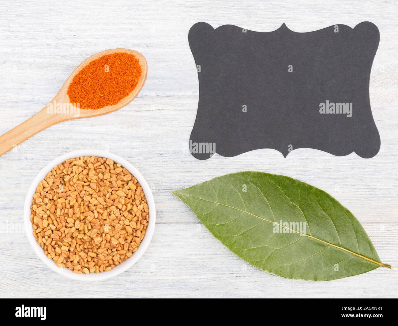 Ground red chili in spoon, fenugreek, bay leaf, nameplate on a white