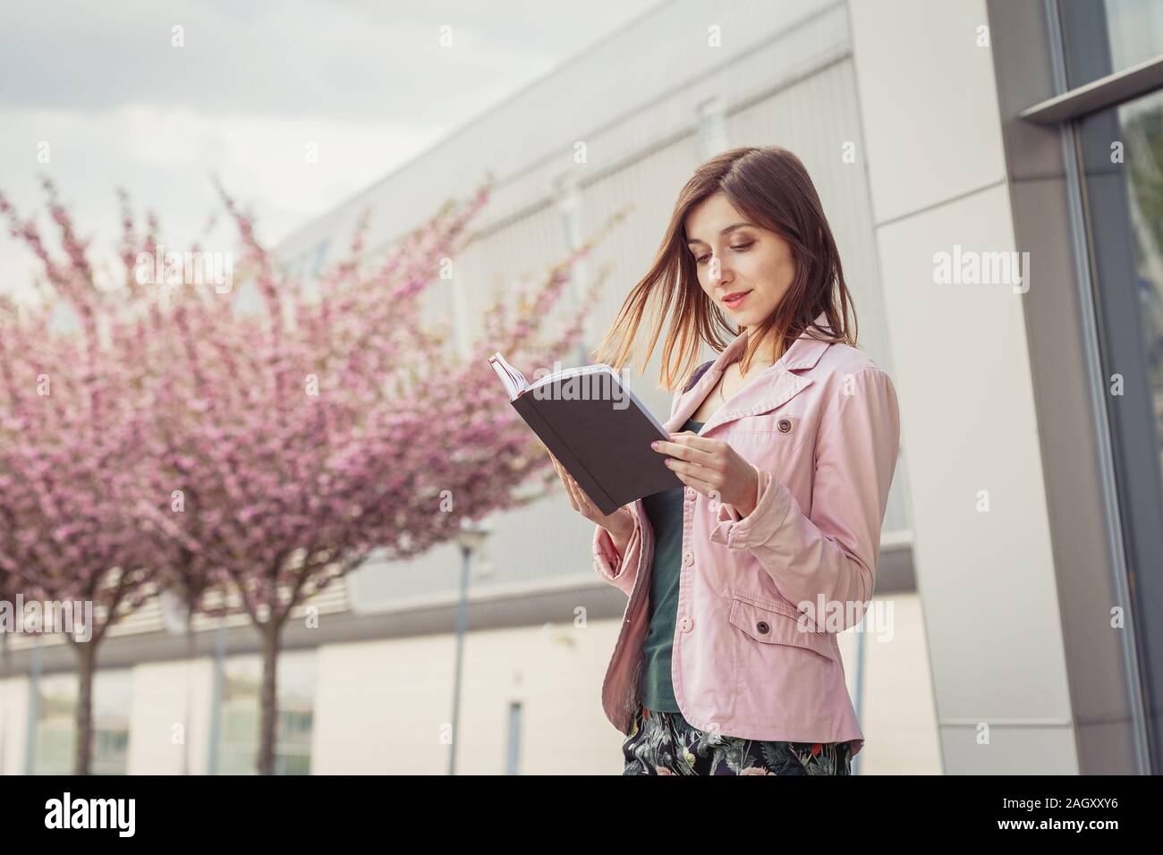 Beautiful young lady checking her day schedule in paper notebook near modern office building Stock Photo