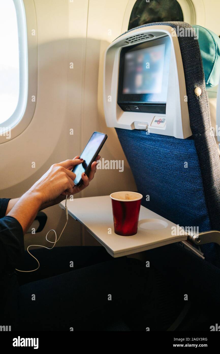 Detail of a woman's hands using mobile phone sitting inside the plane and drinking coffee Stock Photo