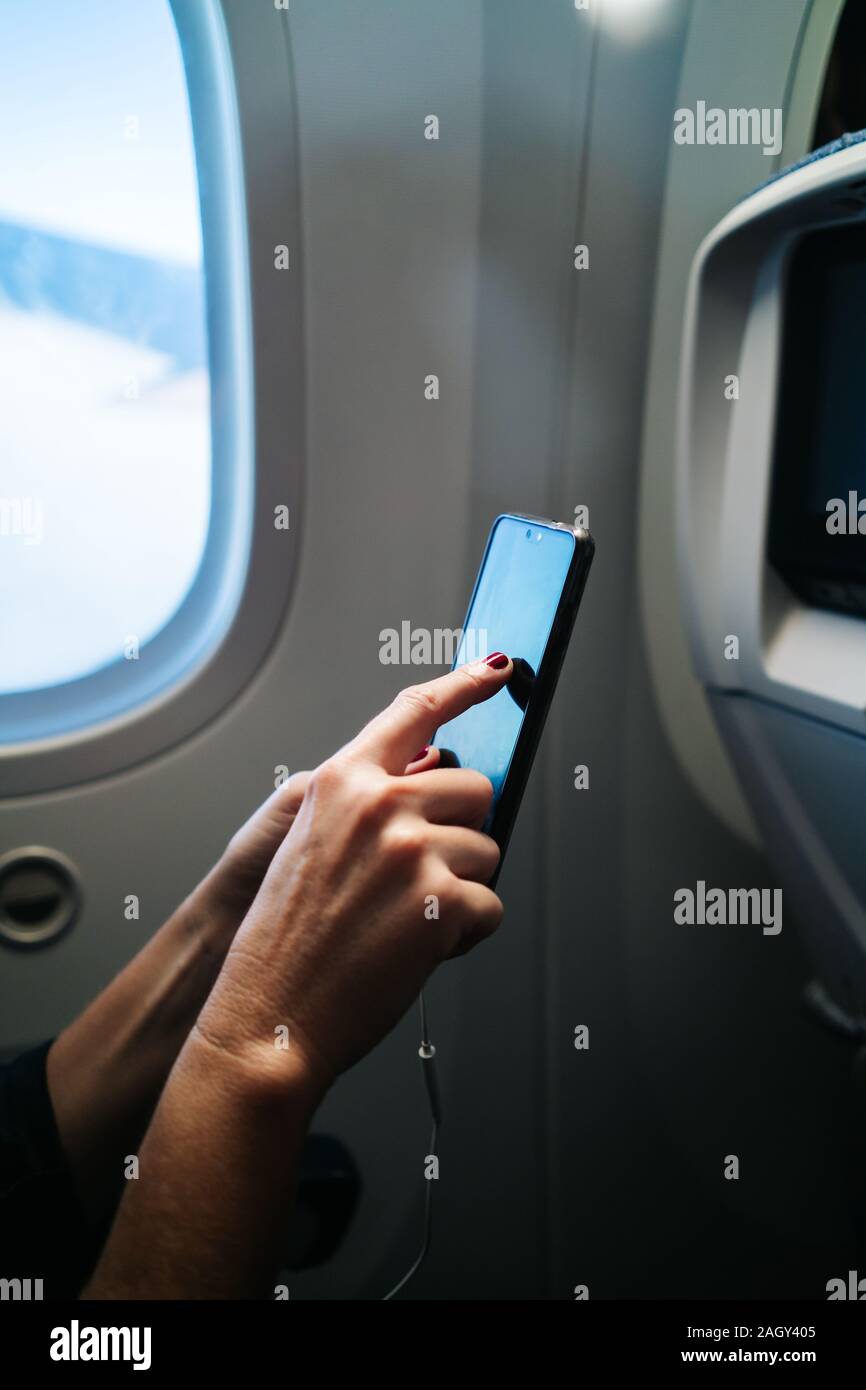 Detail of a woman's hands using mobile phone sitting inside the plane Stock Photo