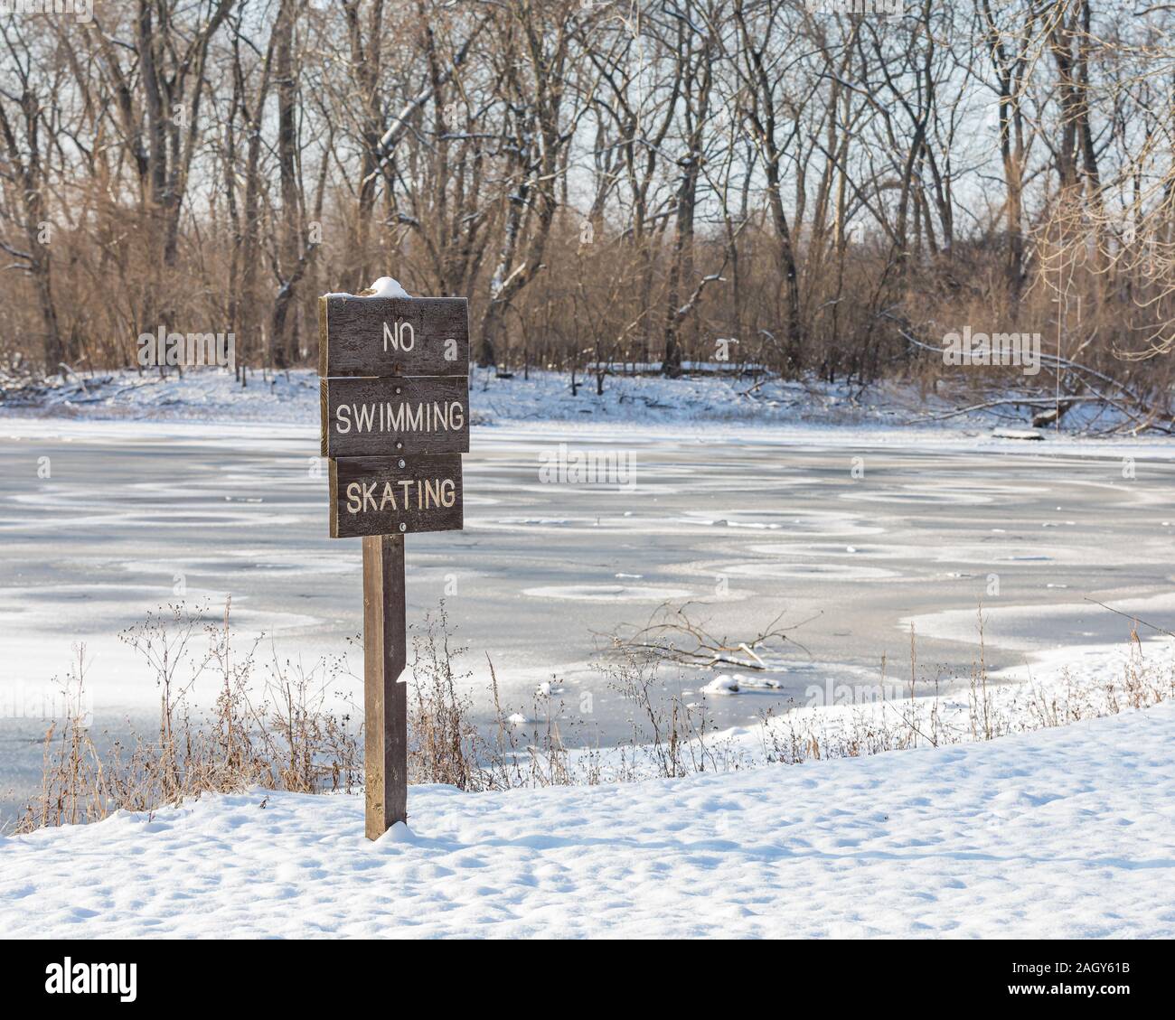 Wooden no swimming, ice skating sign with snow covered ice on frozen lake in background. Concept of winter safety and dangers of thin ice Stock Photo