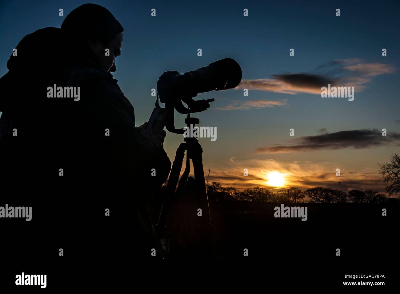 Photographer’s silhouette with the telephoto camera holding mobile phone with visible date on it (22 December, Sunday) against Winter Solstice sunrise. Stock Photo
