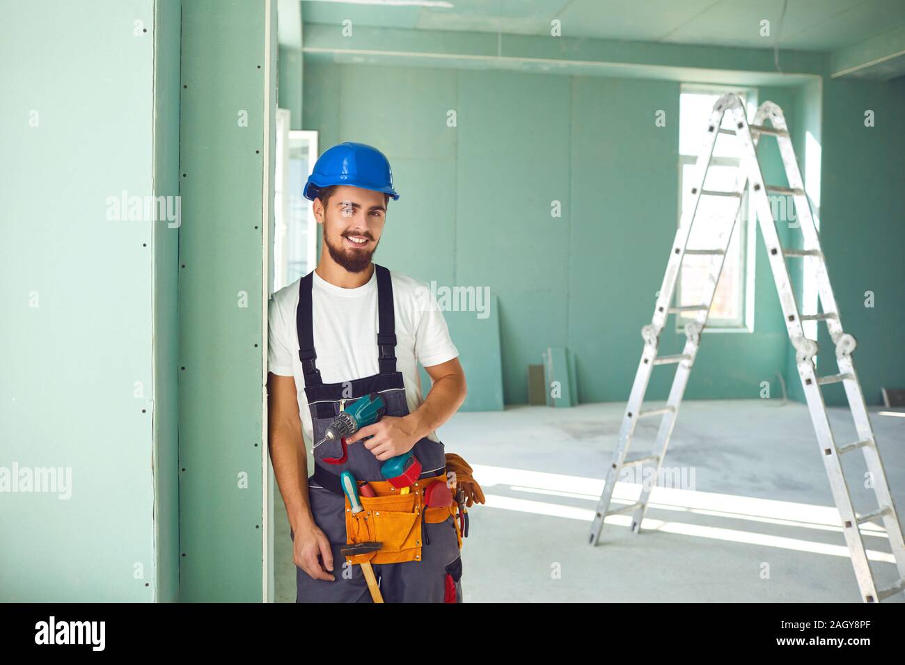 Worker builder installs plasterboard drywall at a construction site office open space. Plasterboard installer. Stock Photo
