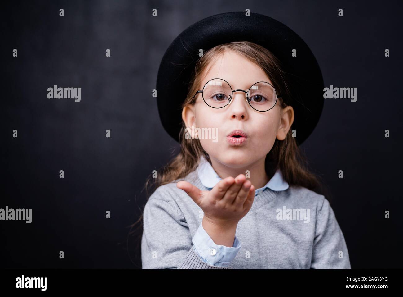 Adorable little girl in smart casualwear and eyeglasses giving you air kiss Stock Photo