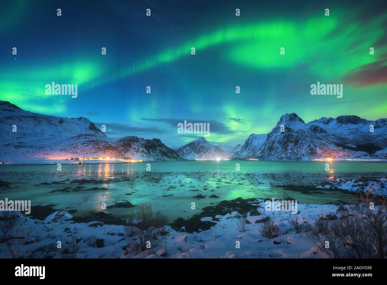 Aurora borealis over the sea coast, snowy mountains and city Stock Photo