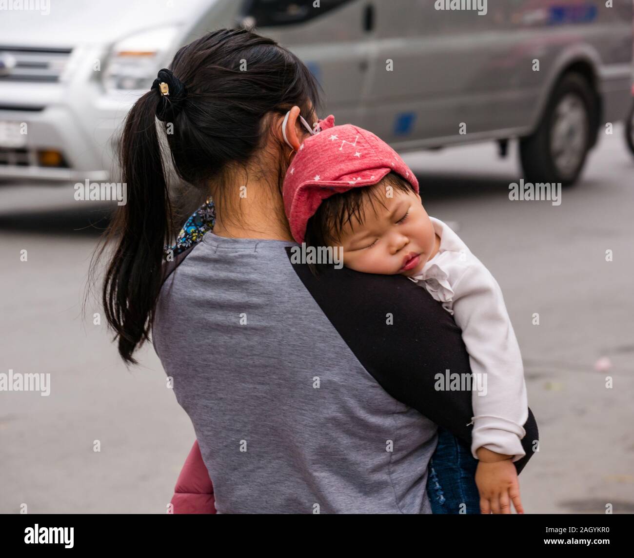 Vietnamese woman carrying sleeping baby on street, Hanoi, Vietnam, Asia Stock Photo