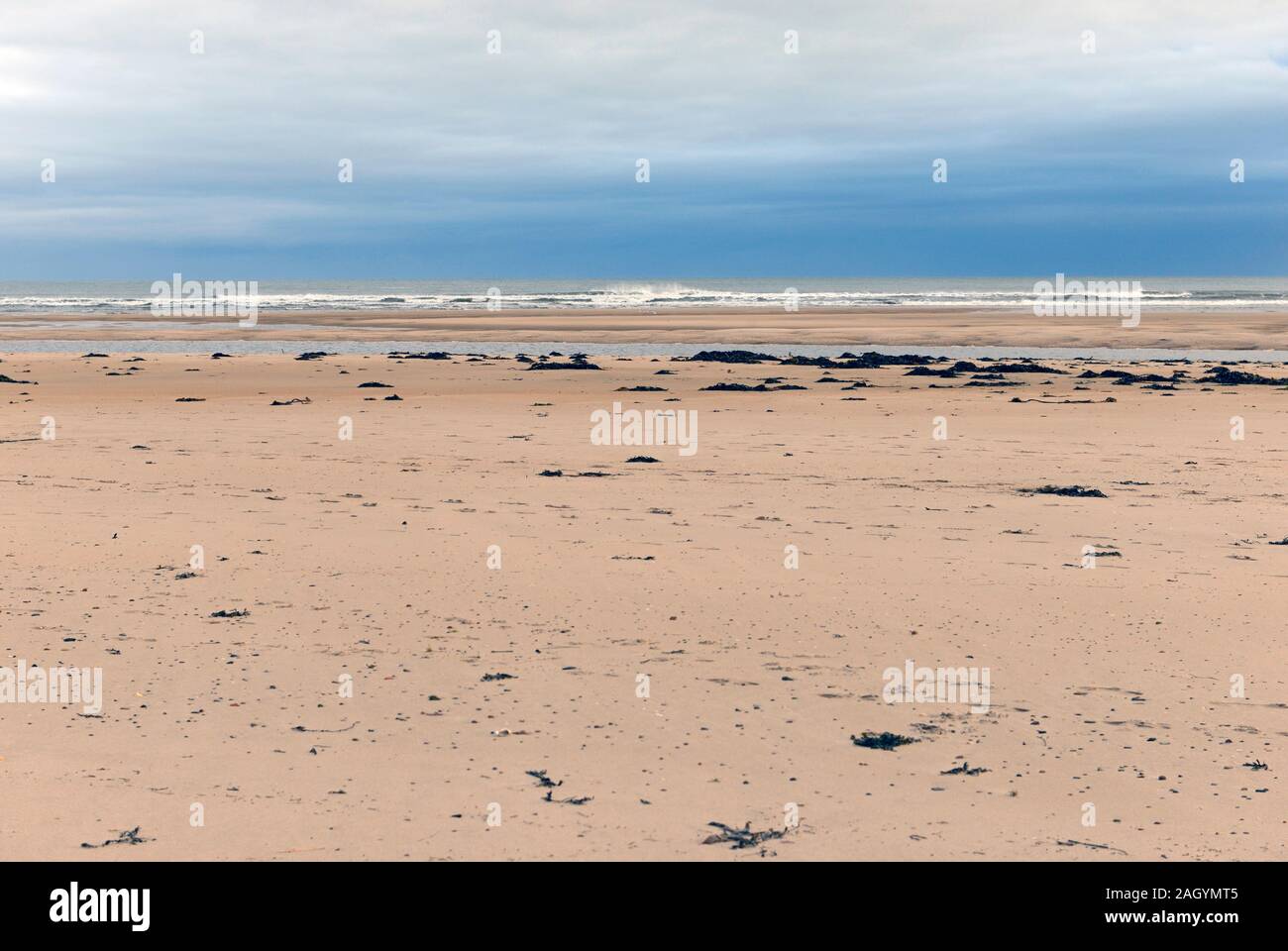 A large expanse of beach stretches out to the distant water at low tide on Alnmouth beach, Northumberland, as a storm has passed over on the horizon. Stock Photo