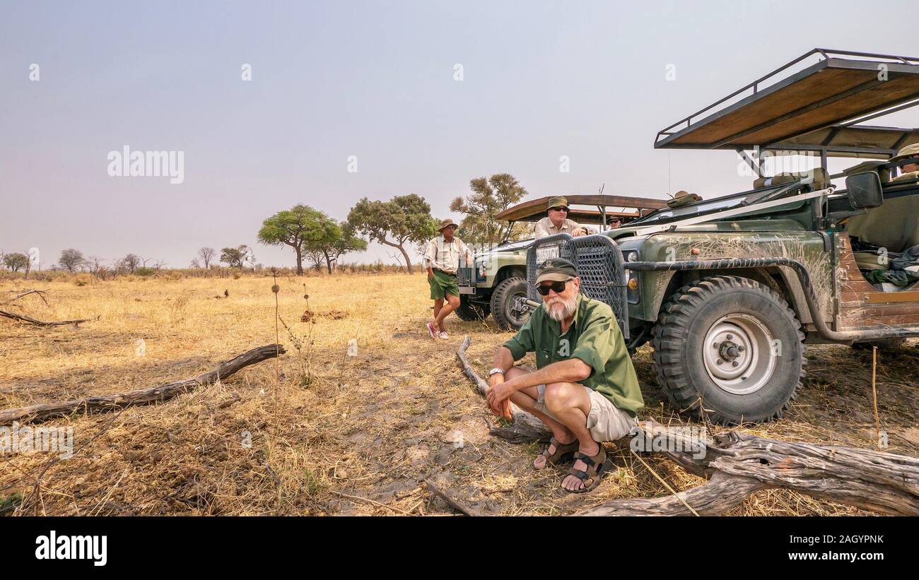 An African safari, with two safari guides and a guest taking a break outside of their jeep vehicles during a photo safari game drive. Stock Photo