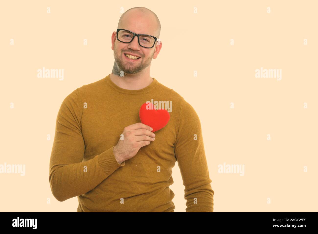 Young happy bald muscular man smiling while holding red heart against chest ready for Valentine's day Stock Photo