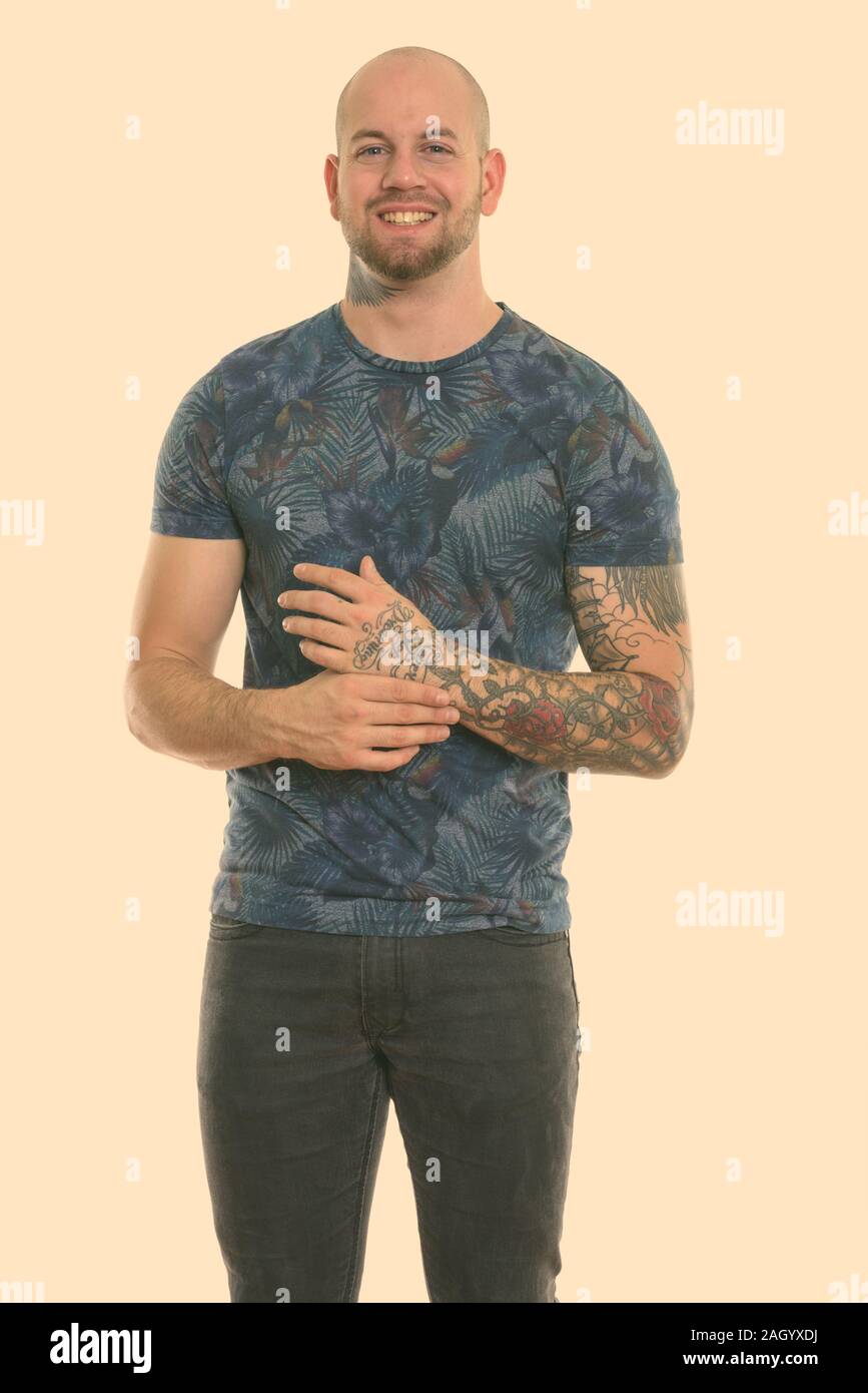Studio shot of young happy bald muscular man with tattoos smiling and ...