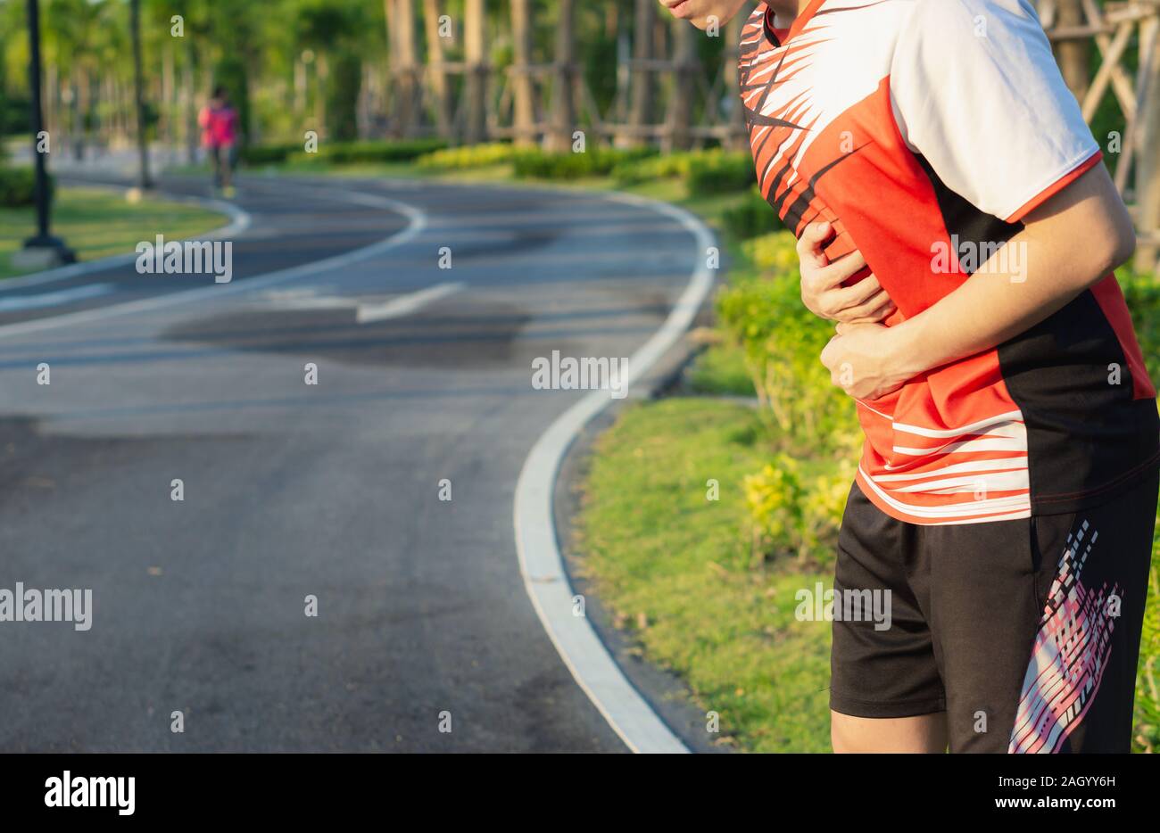 Sport man holding abdomen with his hands in stomach pain after running workout at park. Health