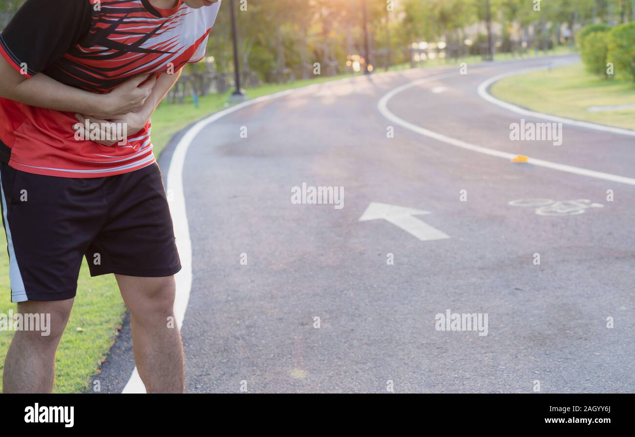 Sport man holding abdomen with his hands in stomach pain after running workout at park. Health