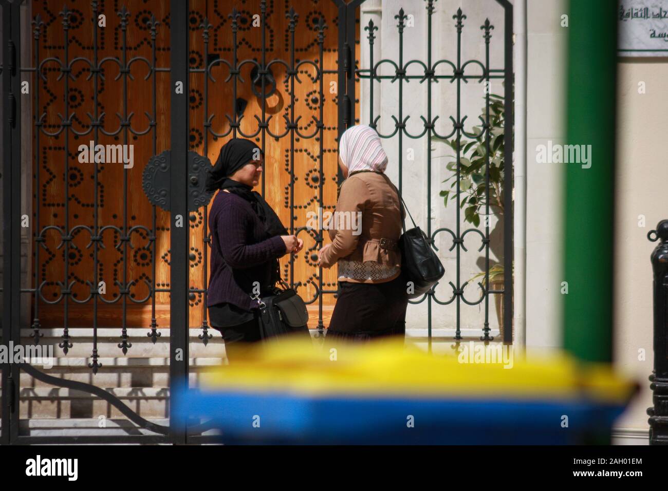 Two Tunisian women with covered hair are having a friendly chat in front of the metal gate in Sousse, Tunisia Stock Photo