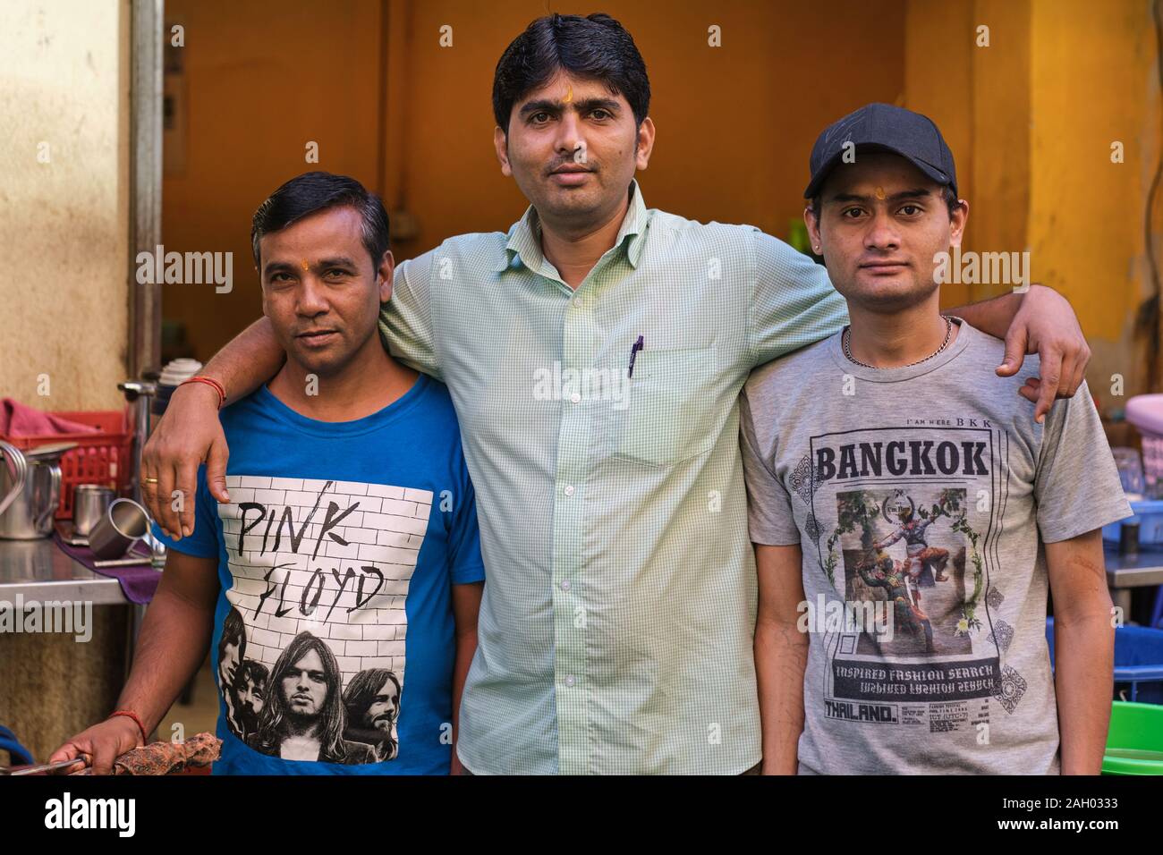 Outside a small Indian restaurant in Pahurat / Phahurat ('Little India'), Bangkok, Thailand, two employees in natty T-shirts flank an Indian customer Stock Photo