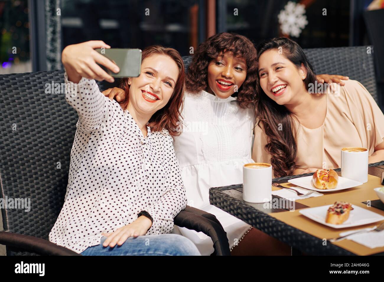 Multi-ethnic happy group of friends sitting at cafe table and posing ...
