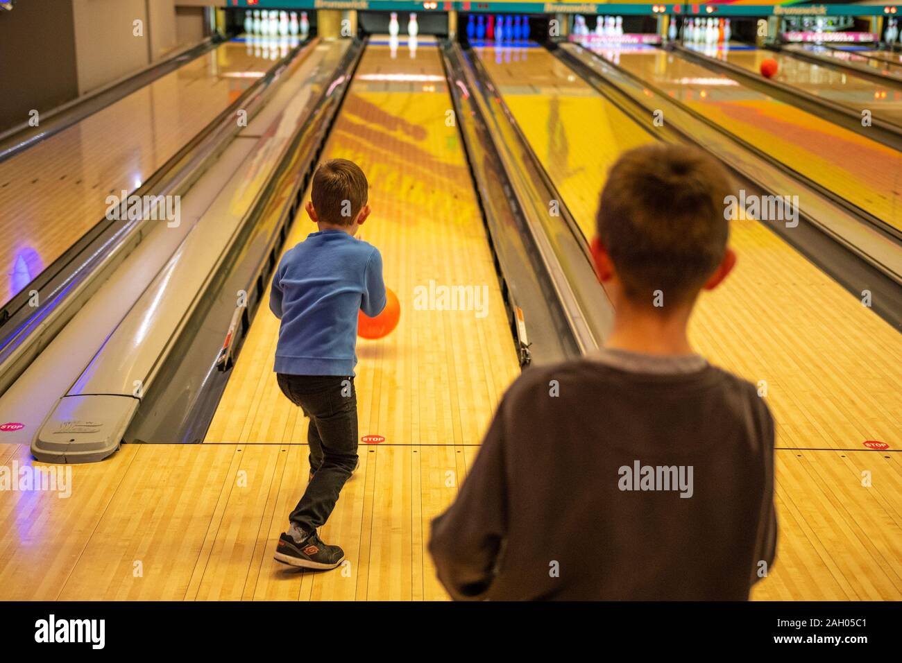 Beautiful scenery of school kids playing bowling at the sport club, kid throwing rolling bowling ball to target Stock Photo
