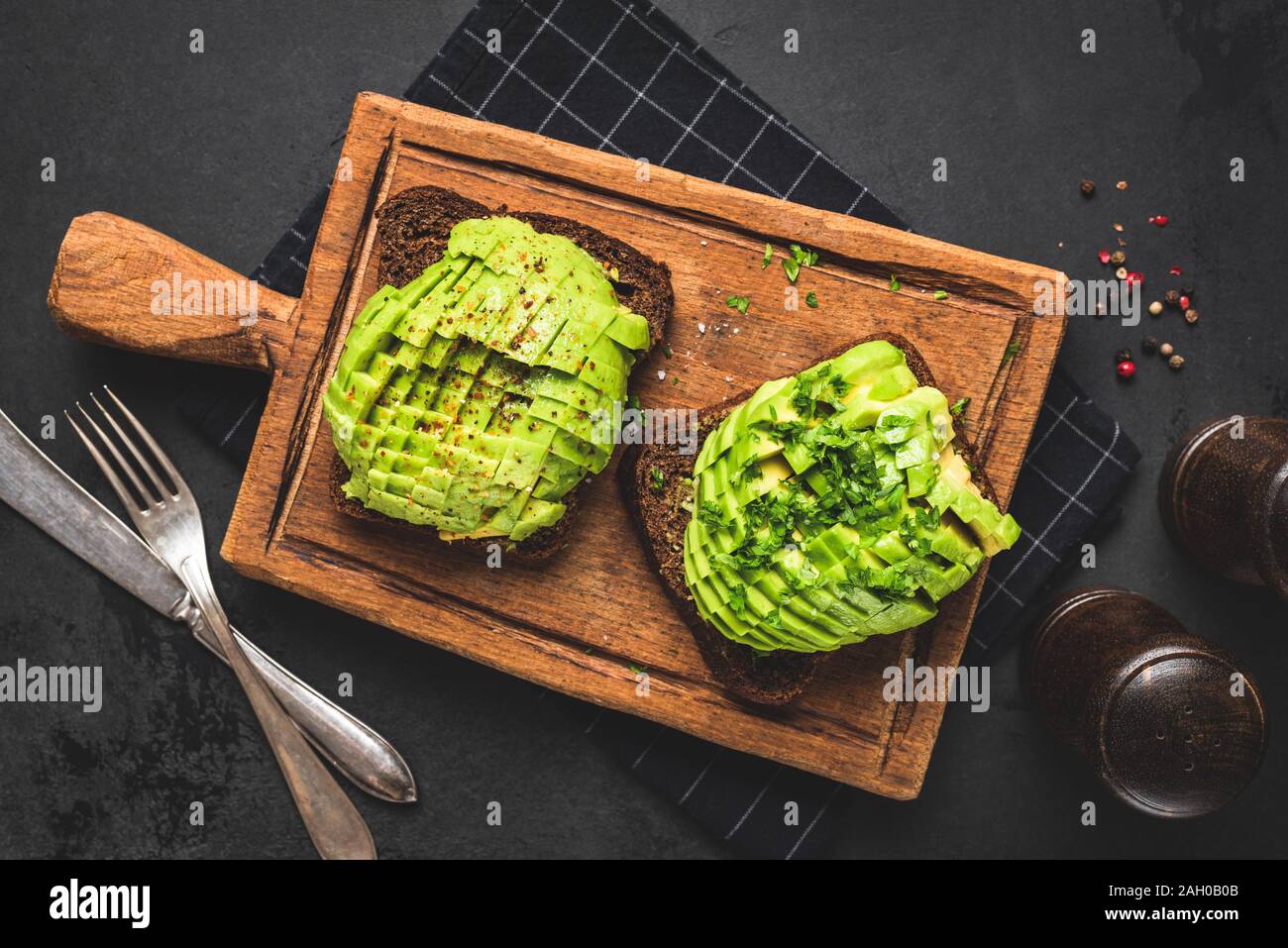 Rye bread toast with avocado and herbs on wooden board, black background. Table top view. Healthy vegan food Stock Photo