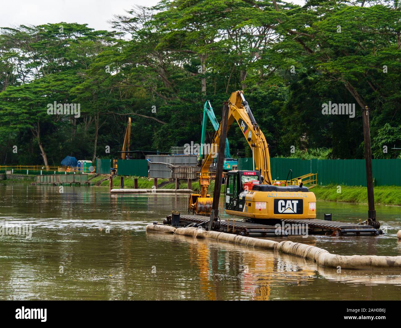 A yellow excavator / bulldozer performing dredging work in a canal / river in a scenic tropical rainforest / jungle habitat in Singapore, South-East A Stock Photo