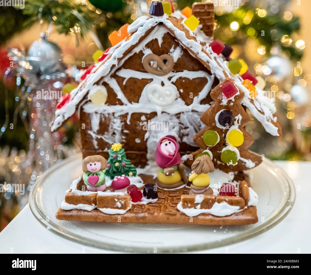 Selective focus on candy characters standing in front of a homemade and home decorated ginger bread house on a white table Stock Photo