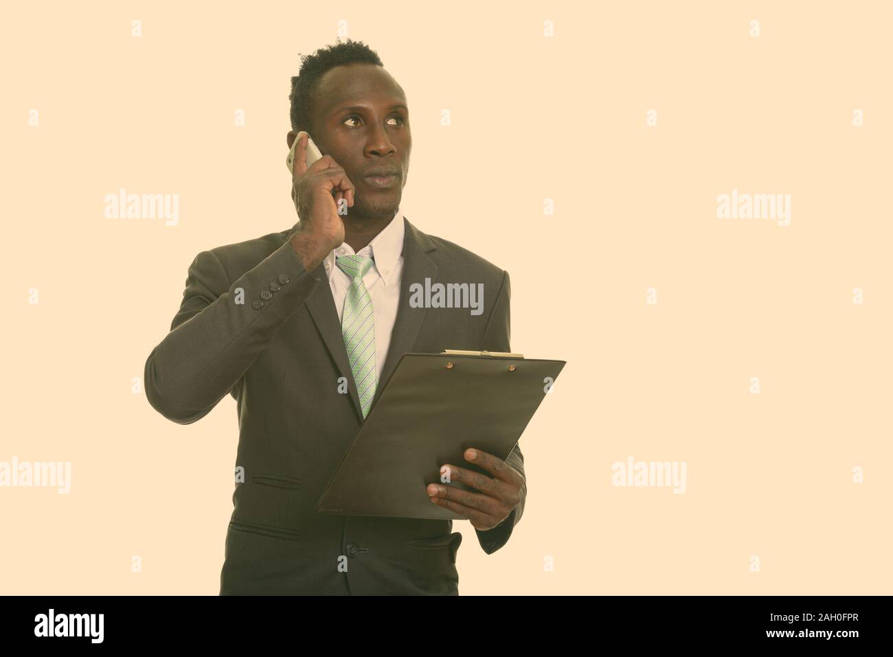 Thoughtful young black African businessman talking on mobile phone while holding clipboard Stock Photo
