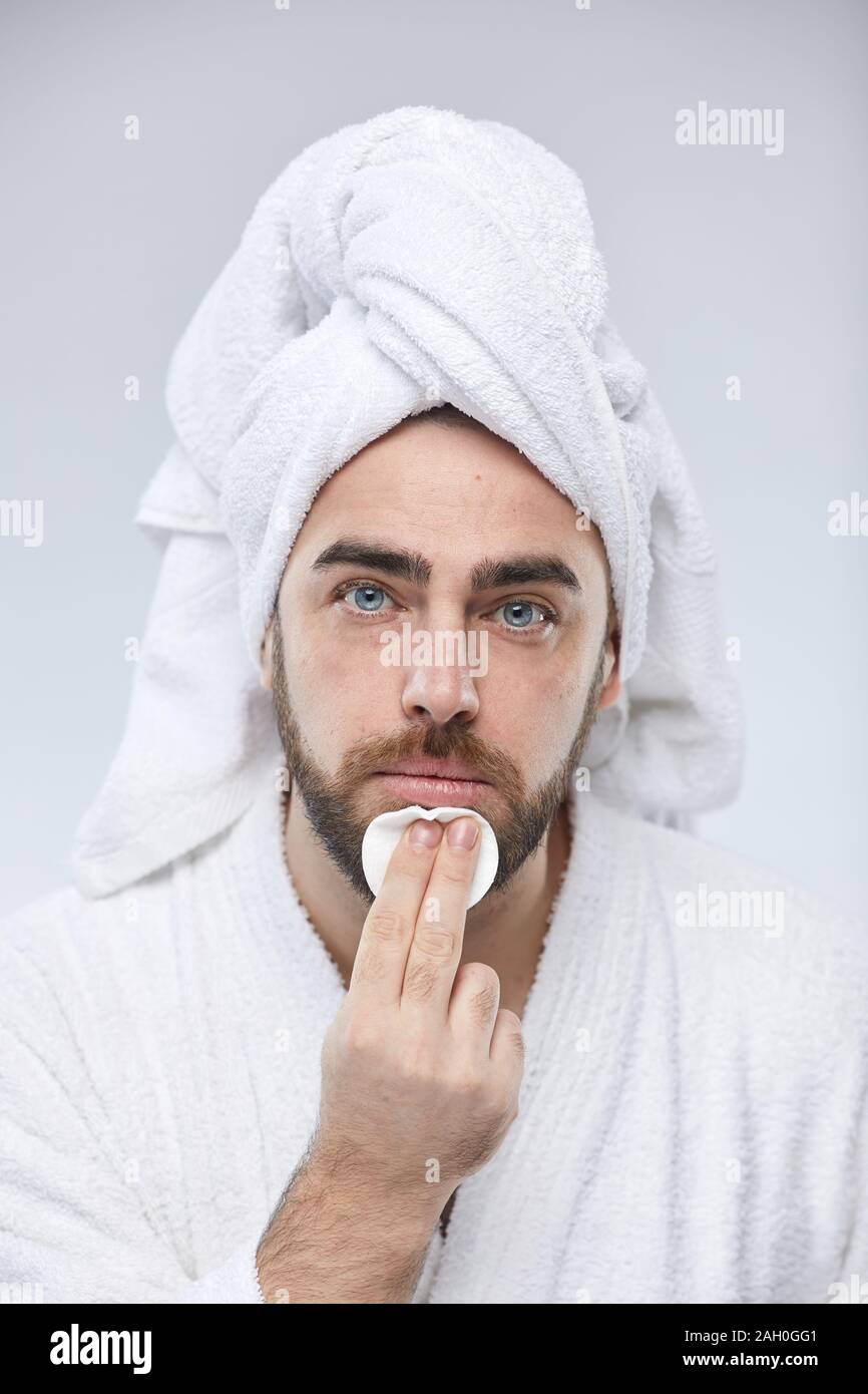 Vertical close up portrait of handsome young man applying toner on face  with cotton pad looking at camera Stock Photo - Alamy
