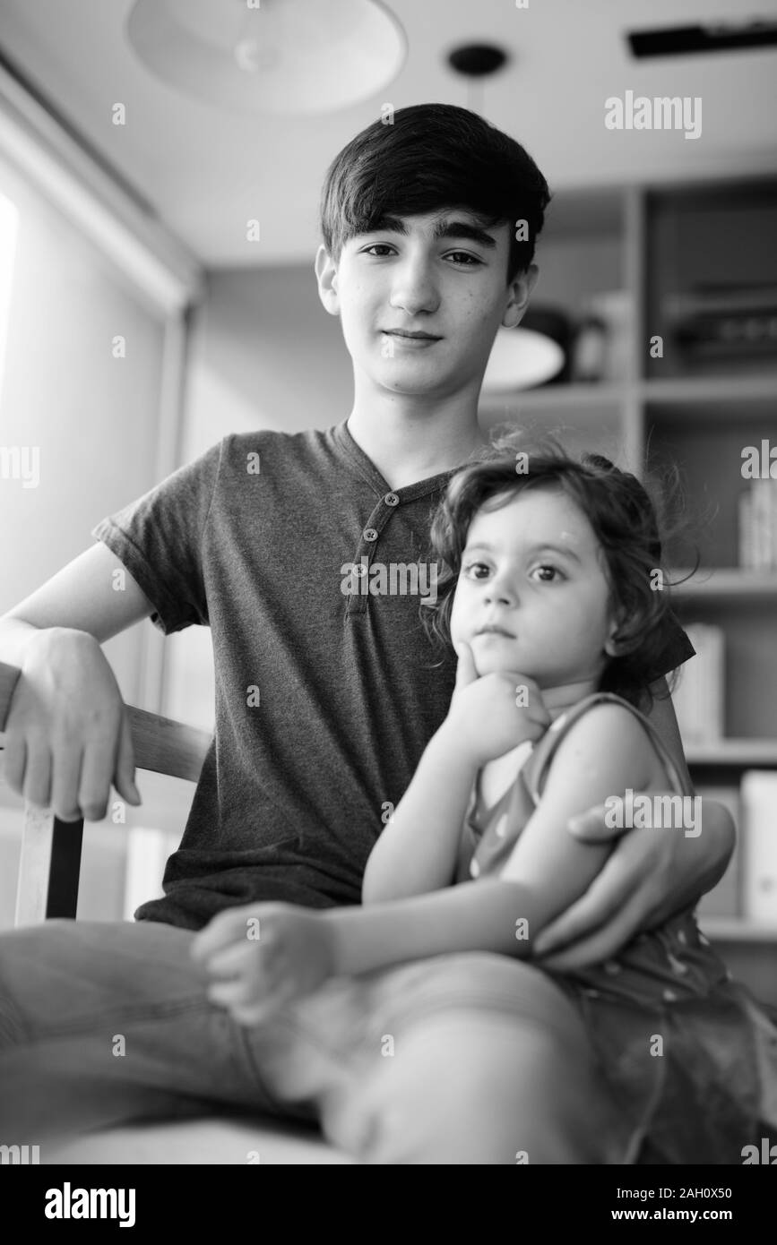 Young handsome Iranian teenage boy with little sister relaxing at home Stock Photo
