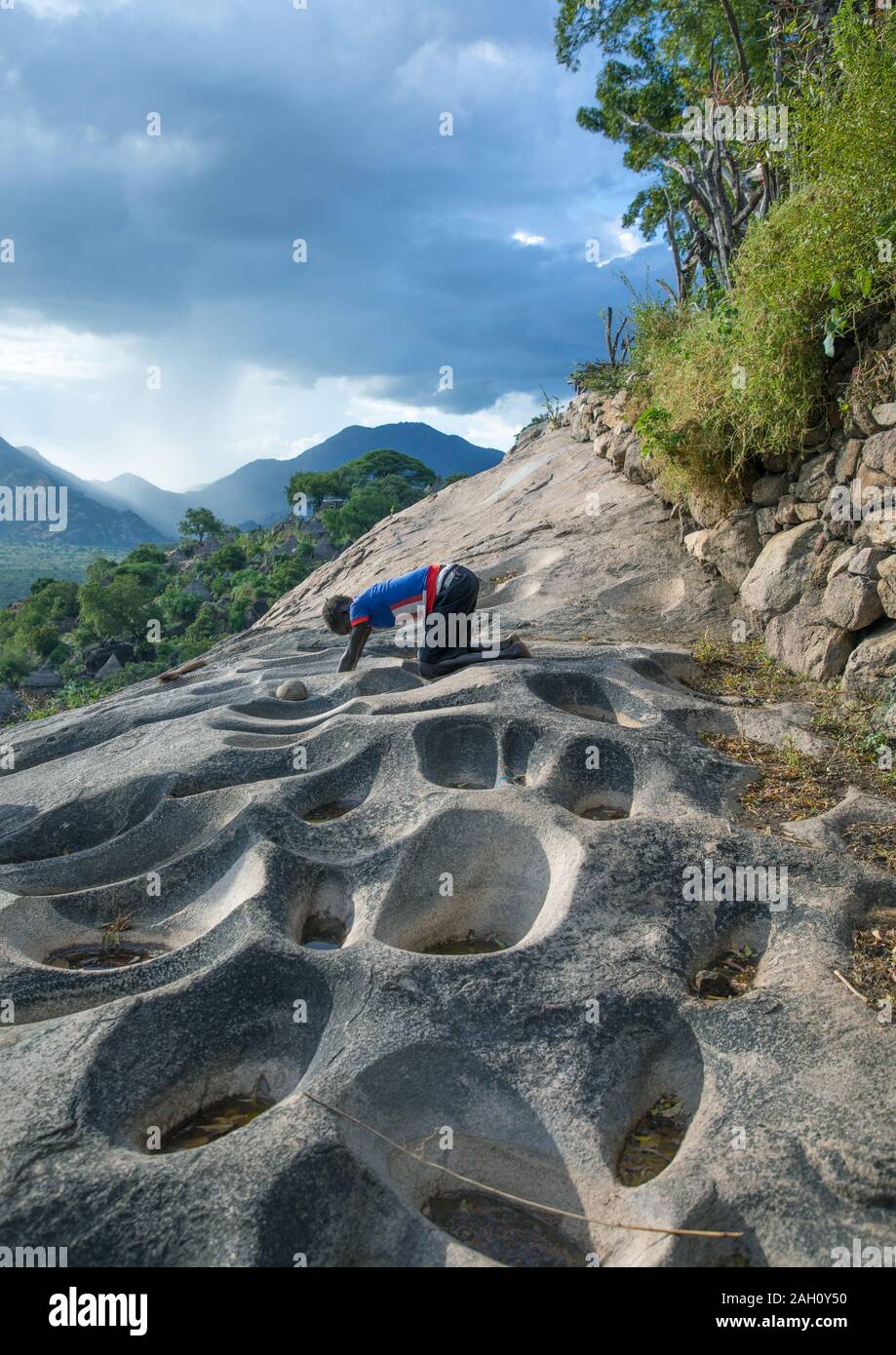 Lotuko tribe woman grinding grains in a hole in the rock, Central