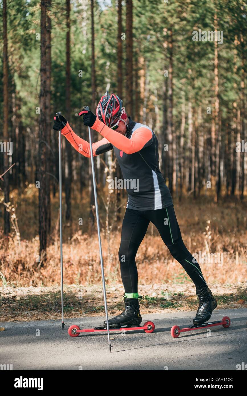 Training an athlete on the roller skaters. Biathlon ride on the roller skis  with ski poles, in the helmet. Autumn workout. Roller sport. The athlete  Stock Photo - Alamy